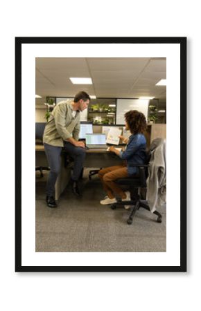 Diverse coworkers reviewing printed report in open-plan office, with laptop and monitors