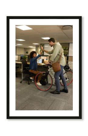 High-fiving diverse colleagues exchanging greetings in modern office, featuring bicycle and laptops