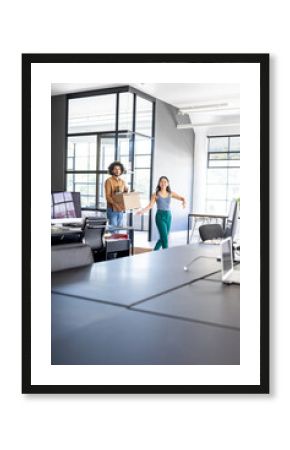Colleagues carrying box and smiling while moving into modern office space