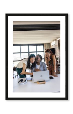 Diverse team celebrating success while looking at laptop in modern office