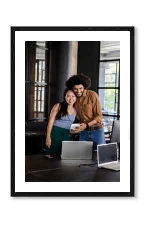 Diverse colleagues celebrating success in modern office, smiling and holding tablet together