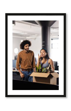 Diverse colleagues discussing office move while unpacking box with desk lamp and plant, copy space