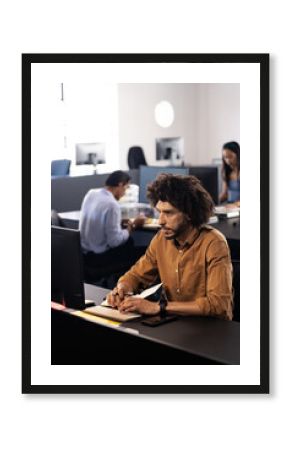 Focused man working at computer in modern office with diverse colleagues nearby