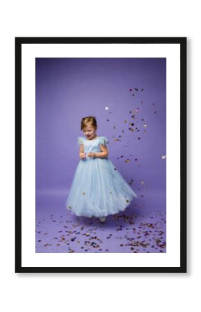 a cheerful little girl in a blue princess dress dances on a purple background with a copy of the space