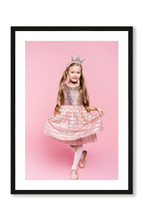 full length of cheerful little girl in dress and crown posing on pink