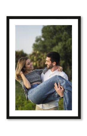 Vertical shot of a Spanish Caucasian couple in the park, him princess carrying her