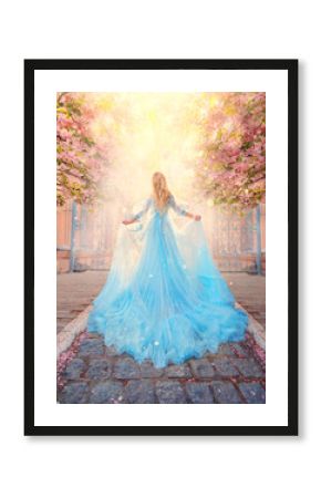 Art photo fantasy woman princess goes to meet light sun along spring street. Pink flowers sakura tree outdoor. Blue lush fairy dress, long train. Silhouette girl goddess, back view. Queen blond hair