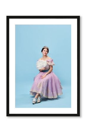 Shyness. Young elegant girl in lilac color medieval dress as young queen or princess on blue background. Eras comparison, beauty, art, emotions and vintage fashion style