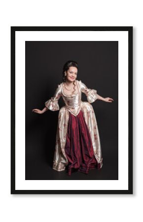 Beautiful smiling woman in rococo style medieval dress standing against dark background