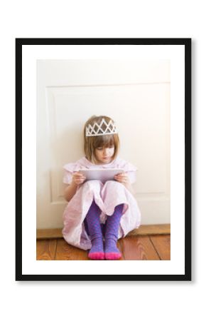 Little girl dressed up as a princess looking at digital tablet
