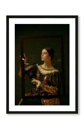 Portrait of a girl wearing a princess or countess dress over dark studio. portrait through picture frame