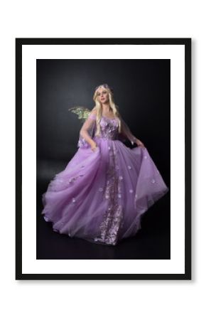 full length portrait of a blonde girl wearing a fantasy fairy inspired costume,  long purple ball gown with fairy wings,   standing pose on a dark studio background.