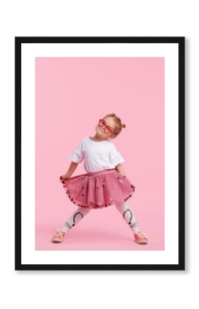 Happy childhood. Funny child girl in tulle skirt jumping and having fun isolated on pink background. Celebrating a vibrant carnival for kids, birthday party. True emotions. Space for text