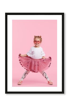Happy childhood. Funny child girl in tulle skirt jumping and having fun isolated on pink background. Celebrating a vibrant carnival for kids, birthday