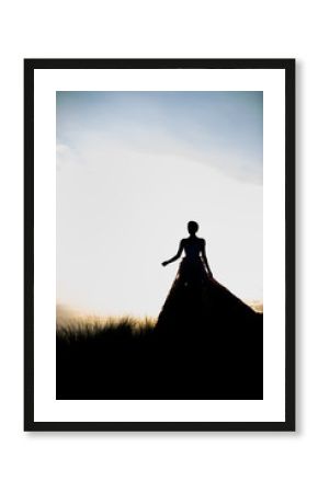 Wide shot of a fairytale princess dark silhouette against a clear sky with a sunrise of a female in a ballgown or wedding dress.