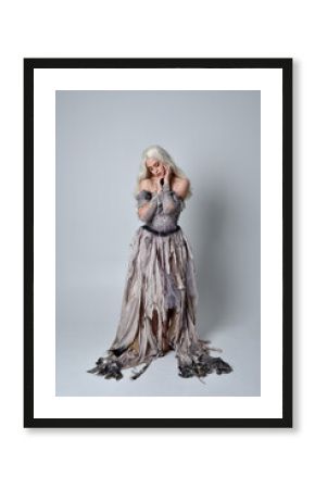 full length portrait of blonde girl wearing long torn, old wedding gown. standing pose on a studio background.