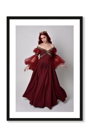 Portrait of a beautiful woman with red hair wearing  a  flowing Burgundy fantasy gown and golden crown.  full length standing pose, isolated against a studio background 