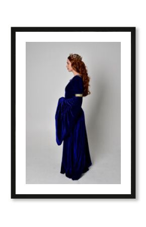 Full length portrait of  girl wearing long blue velvet gown with golden crown. standing pose with back to the camera, isolated against a studio background.