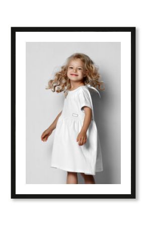 Little blonde curly positive princess girl in white casual dress and sneakers standing walking with curly hair over grey wall