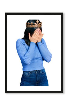 Young brunette woman with blue eyes wearing princess crown with sad expression covering face with hands while crying. depression concept.