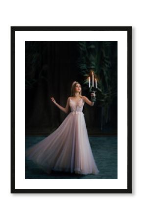 Art photo of medieval girl princess walks runs in dark gothic room. Woman queen is holding candlestick with burning candles in hand. Pink purple dress fly in motion. long blonde hair gold royal crown