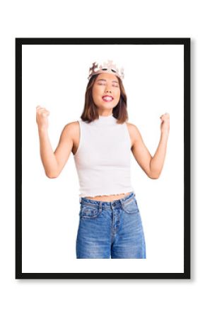 Young beautiful chinese girl wearing princess crown very happy and excited doing winner gesture with arms raised, smiling and screaming for success. celebration concept.