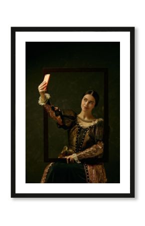 Portrait of a girl wearing a princess or countess dress with mobile phone over dark studio making selfie photo