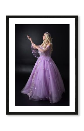 full length portrait of a blonde girl wearing a fantasy fairy inspired costume,  long purple ball gown with fairy wings,   standing pose  on a dark studio background.