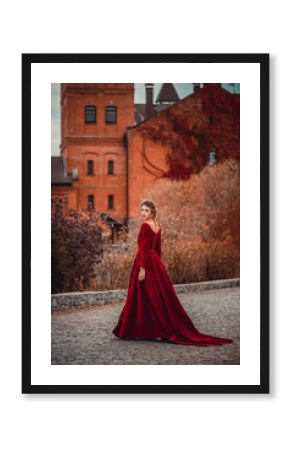 Beautiful girl in a burgundy red dress walking near  old castle on a background of autumn grape leaves in the park, October. Radomyshl