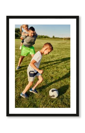 Boy playing soccer by man giving piggyback ride to girl at sports field