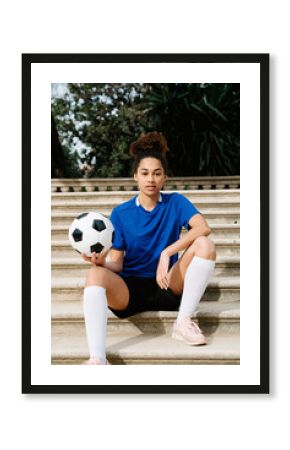 Confident soccer player with soccer ball sitting on steps