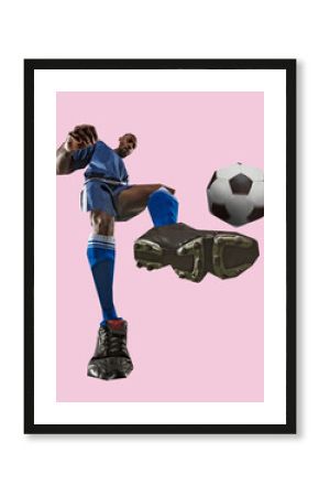 Low angle view of man, soccer player in blue uniform kicking ball mid-air with oversized cleats in surreal cut-out style against pastel pink background. Concept of sport, competition, tournament, game
