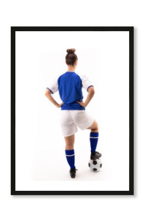 Rear view of biracial young female player with hand on hip standing on soccer ball