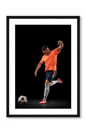 Studio shot of professional male football soccer player in motion isolated on dark background. Concept of sport, goals, competition, hobby, achievements