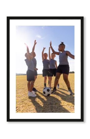 Multiracial elementary schoolboys with arms raised standing on soccer filed against sky