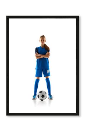 Focused teen girl in blue uniform, soccer player standing with ball, posing isolated on white studio background. Concept of sport, active and healthy lifestyle, childhood, school, hobby