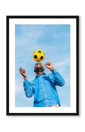 Black man playing with a yellow soccer ball outdoors