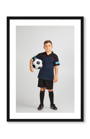 little boy football player in uniform holding ball over studio background. child dreams of becoming a soccer player.