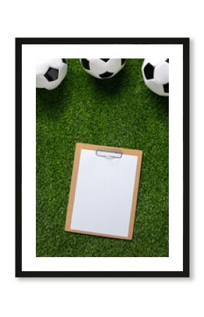 A soccer balls and clipboard on a lush green grassy surface. Top view. Copy space.