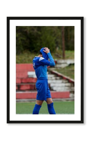 young soccer player in blue suit holds his head in his shirt in despair after losing the match