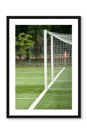 A soccer ball approaches the goal post on a vibrant green field. The well-maintained turf is bordered by trees, creating a lively backdrop for the action taking place under clear skies