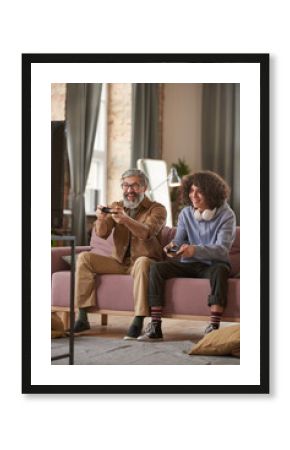 Happy father sitting on sofa and playing video game on TV together with his son at home