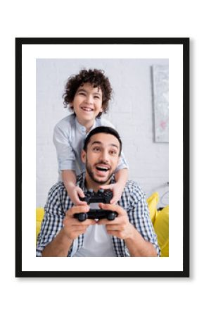 KYIV, UKRAINE - JANUARY 15, 2021: amazed arabian man playing video game together with excited son