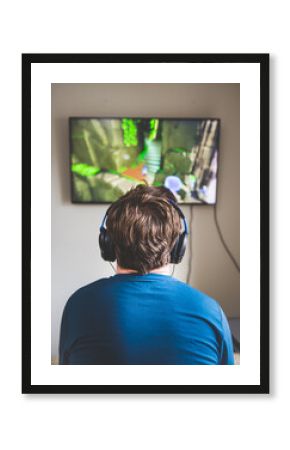 Rear view of boy playing video games with headphones