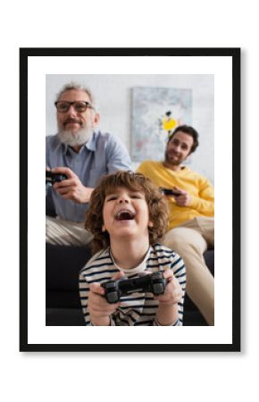 KYIV, UKRAINE - APRIL 12, 2021: Excited kid playing video game near blurred parents