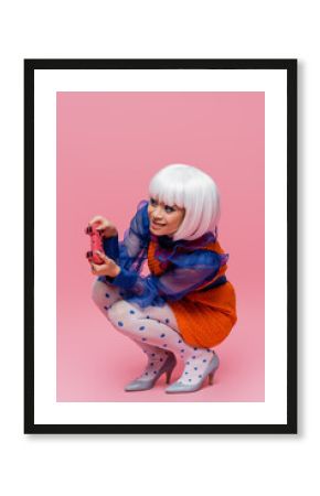 KYIV, UKRAINE - DECEMBER 10, 2020: Smiling asian pop art model playing video game on pink background