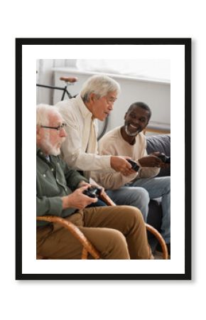 KYIV, UKRAINE - OCTOBER 12, 2021: Focused asian man playing video game with elderly friends at home.