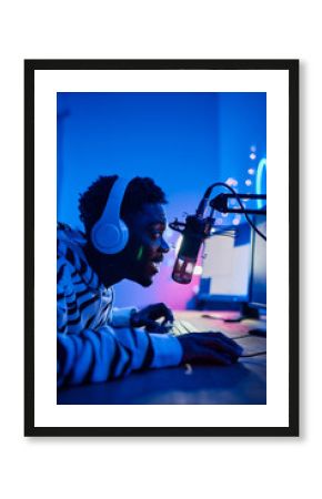 African excited gamer boy in headset speaking in microphone to audience while playing online video game