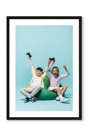 KYIV, UKRAINE - JULY 2, 2021: Excited multiethnic kids holding joysticks on beanbag chair on blue background.