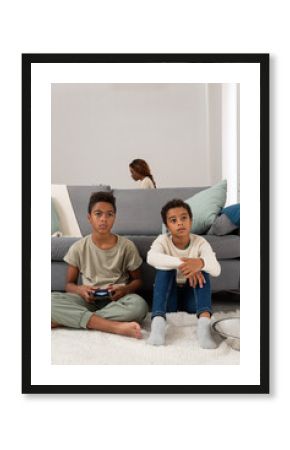 Brothers playing videogame near working mother